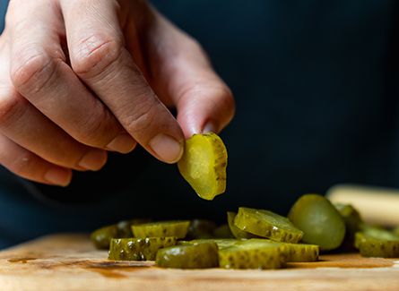 Someone holding pickle off of cutting board