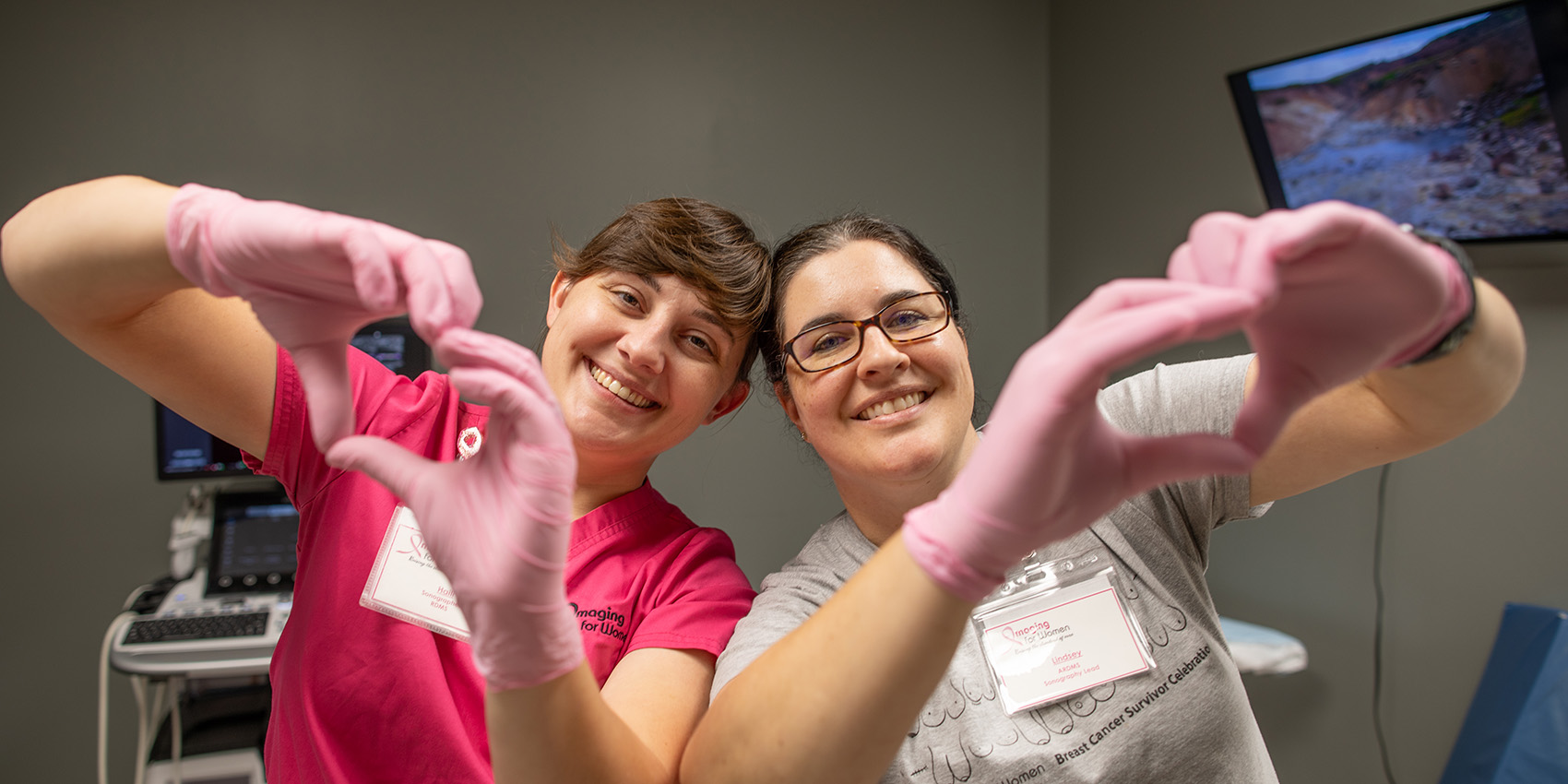 Two radiology techs making hearts with their pink-gloved hands