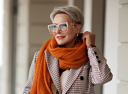 Older woman walking outside, wearing orange scarf and glasses